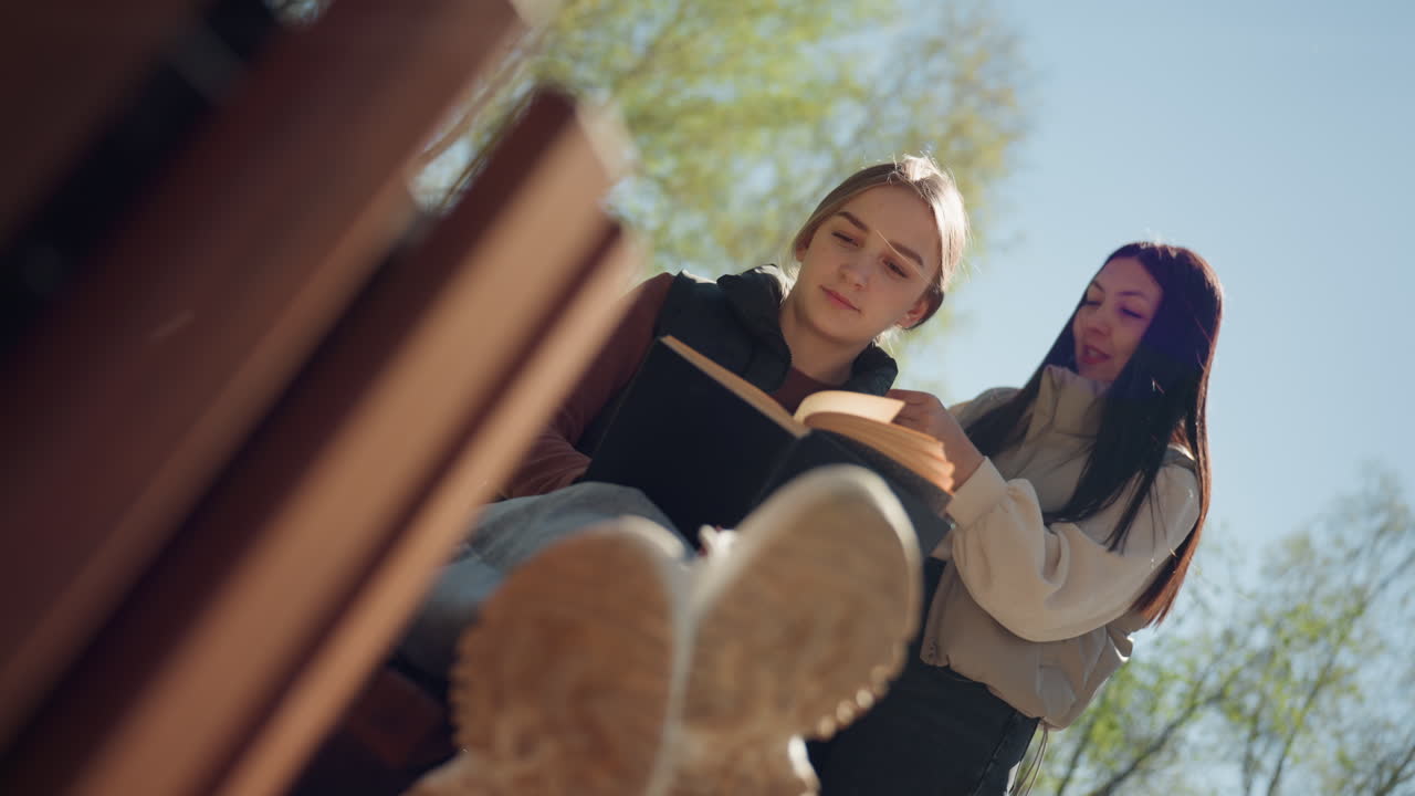 봄을 즐기는 친구들, 친한 동료들과 함께하는 봄 소풍, 아름다운 봄날 야외 캠퍼스 모임, 젊은 여성과 아시아인 친구가 봄에 공원 벤치에 평화롭게 앉아 있어요.