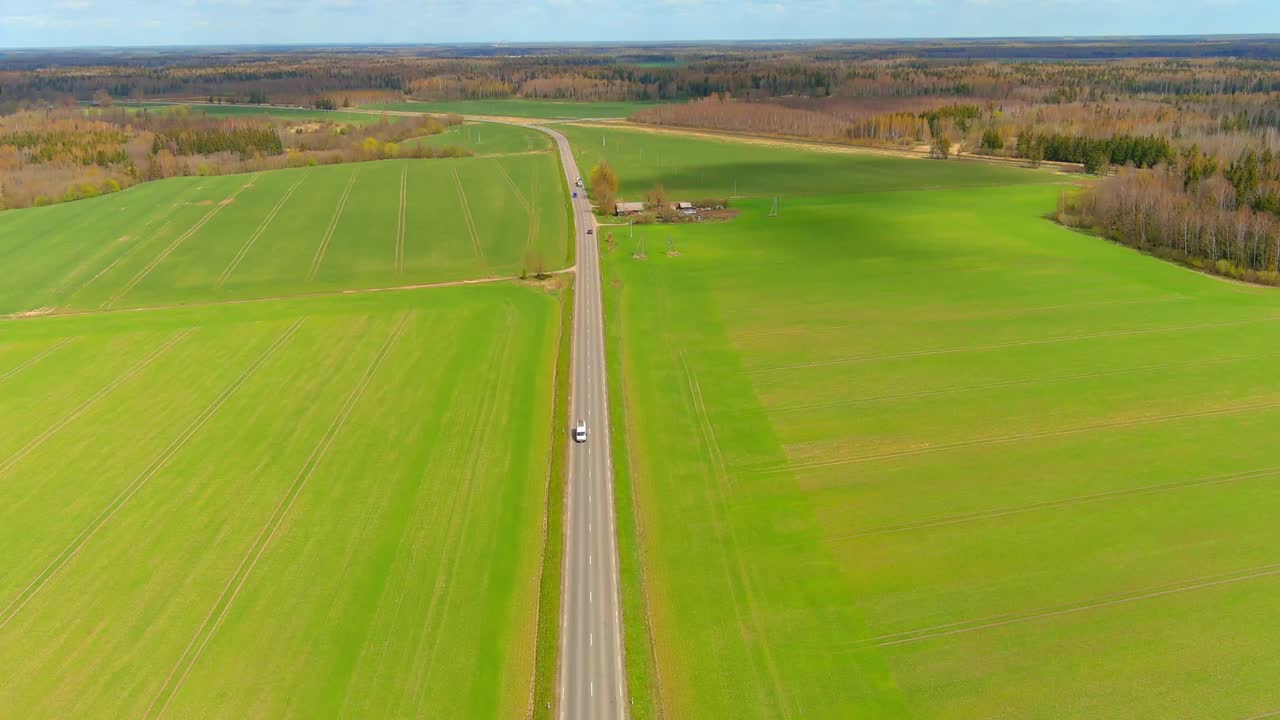 녹색 들판의 형태로 오른쪽과 왼쪽으로 움직이는 자동차가 있는 시골 도로의 공중 드론 전망