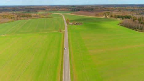 aerial drone view of rural road with cars moving on the right and left in the form of green fields