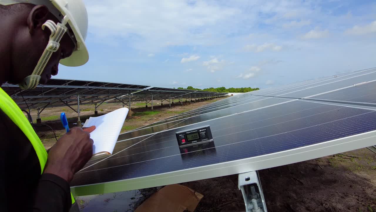 Black male professional engineer technician working on solar panel photovoltaic installation of renewable energy farm checking tilt angle and testing the efficiency in Africa