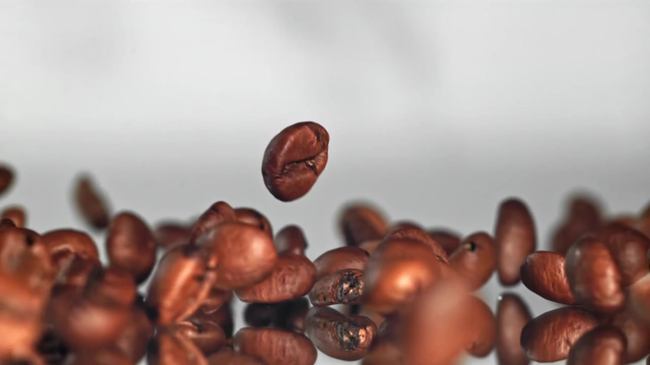 Ristede kaffebønner som faller i sakte film på en reflekterende overflate