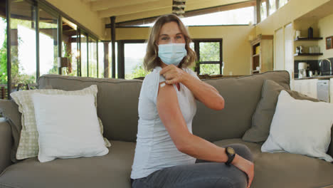 caucasian pregnant woman in face mask showing arm with plaster after vaccination