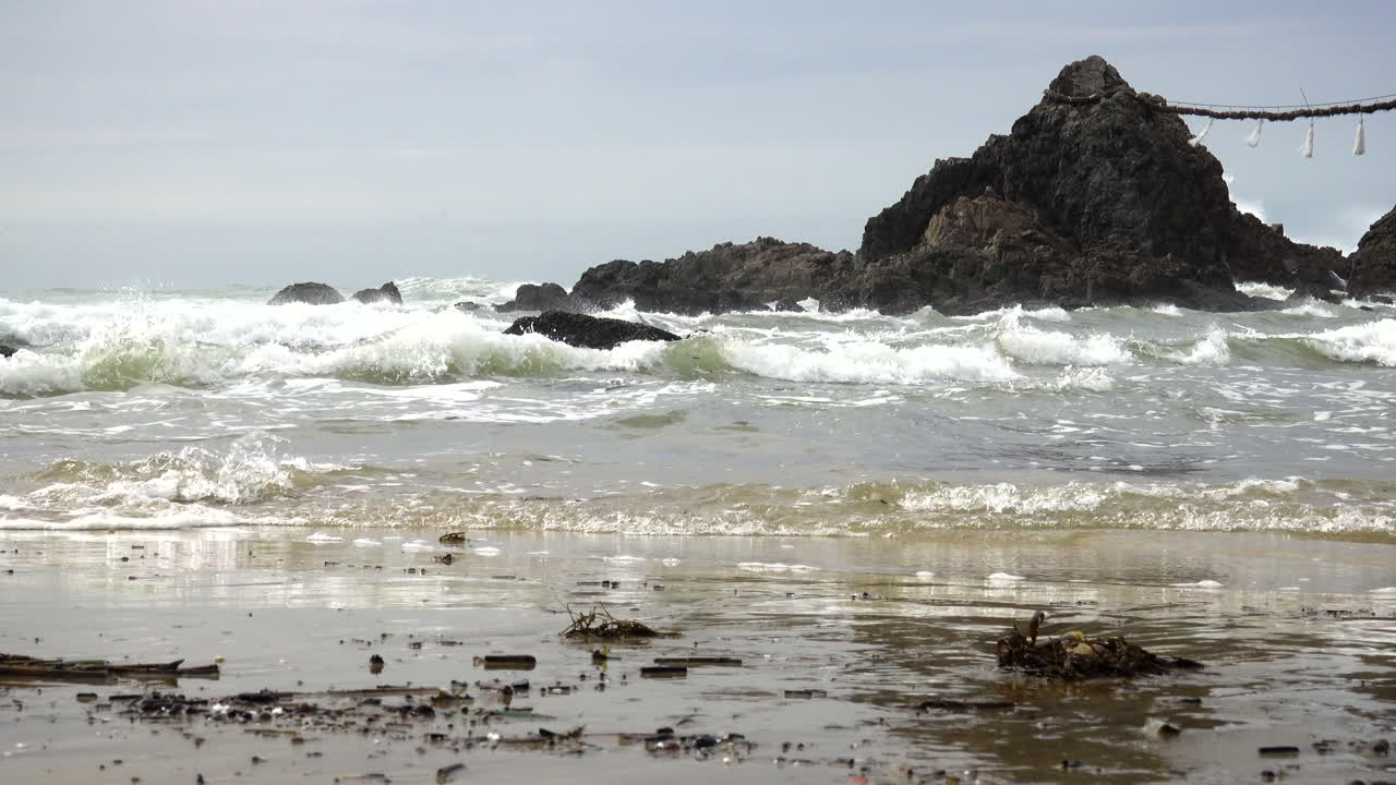 Strong tide with waves white foam hitting the rocks on the shore of a beach during a windy day