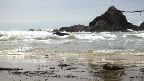 strong tide with waves white foam hitting the rocks on the shore of a beach during a windy day