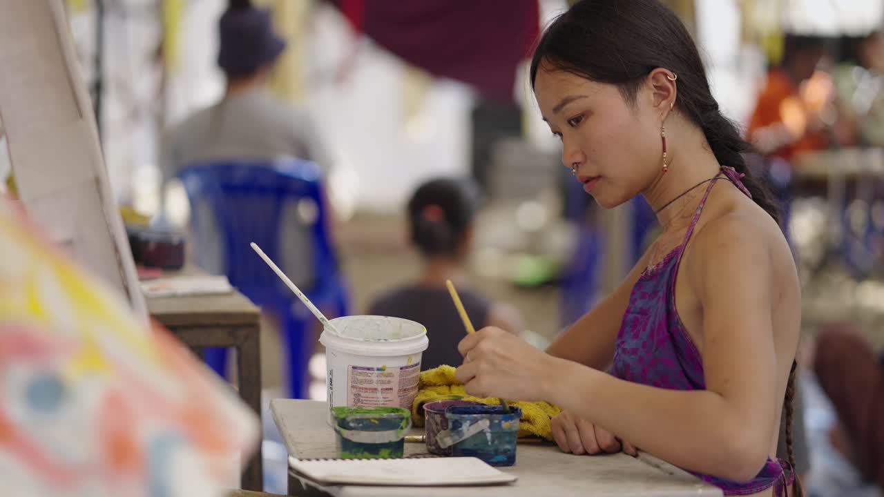 A young woman creating art, concentrating on her painting at an outdoor workshop
