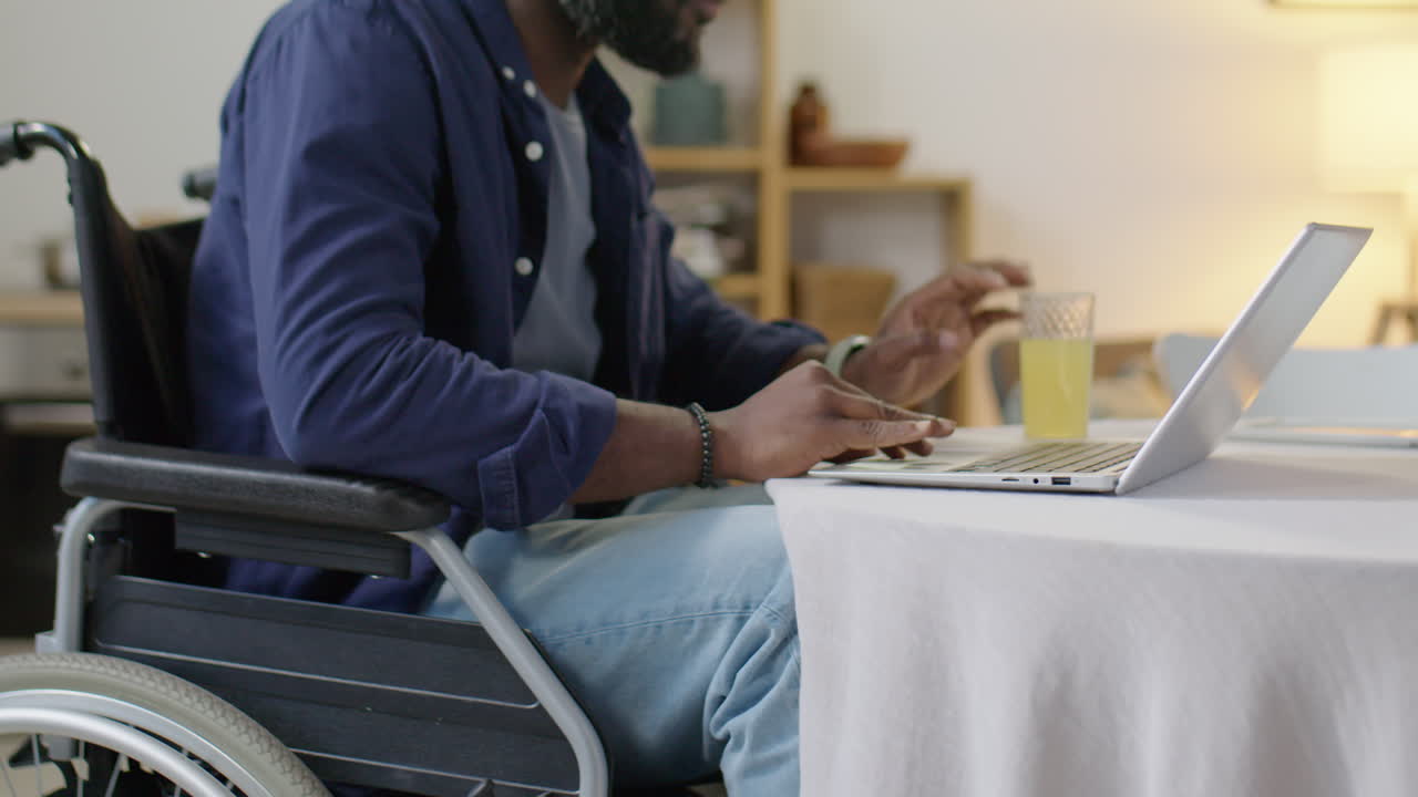 Man in Wheelchair Using Laptop and Drinking Juice at Home