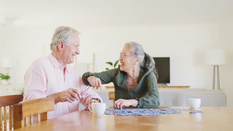 feliz pareja de ancianos diversos sentados a la mesa y haciendo rompecabezas