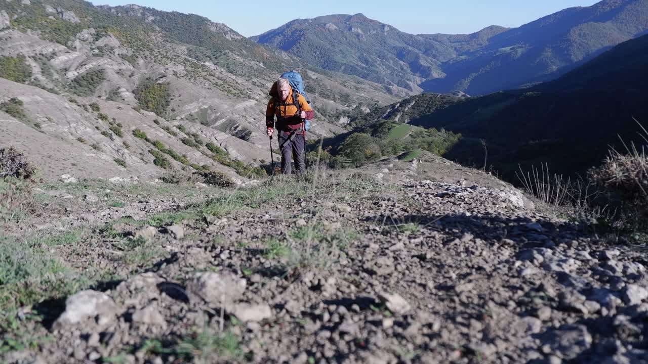 무거운  ⁇ 을 가진 남성 배 ⁇  여행자가 카메라를 향해 산꼭대기를 오르고 있습니다.
