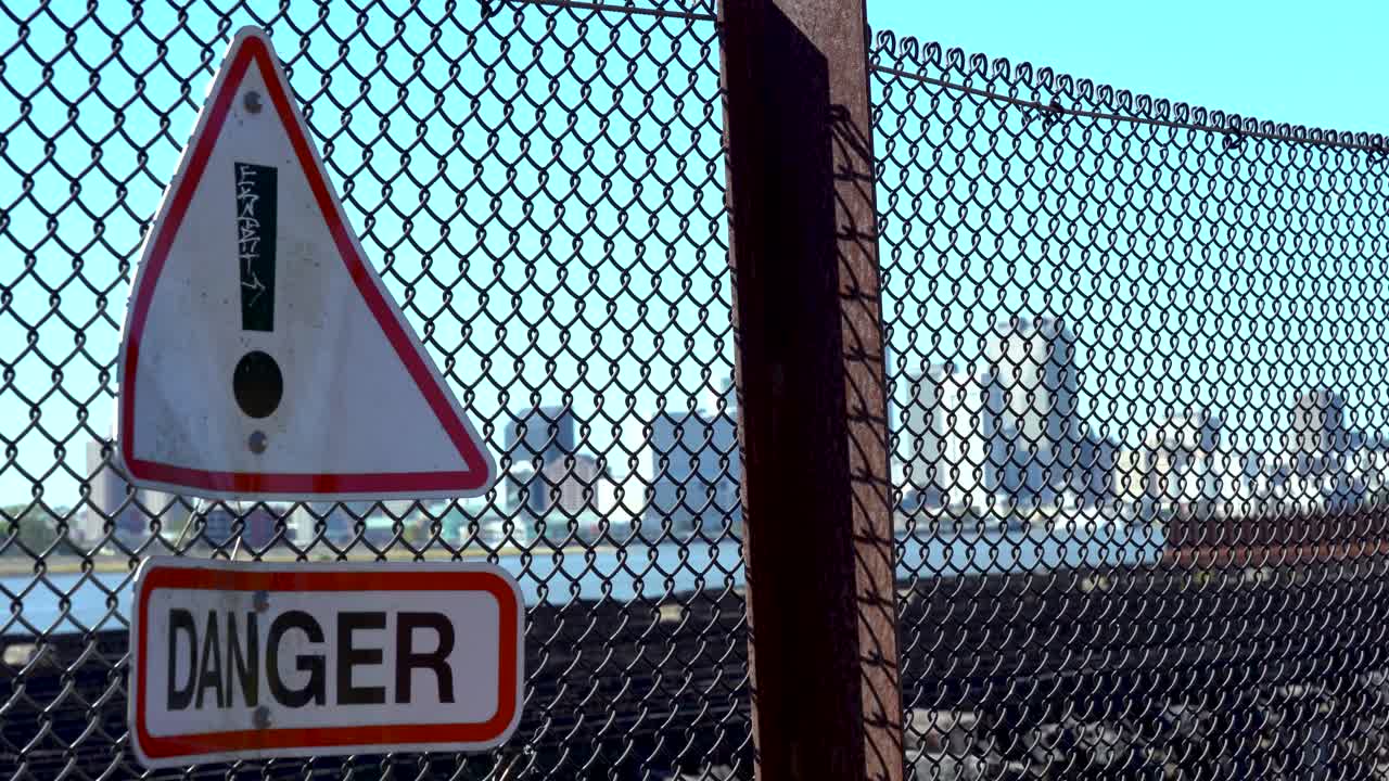 Warning danger sign on rusty chain fence in front of city skyline