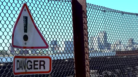 warning danger sign on rusty chain fence in front of city skyline