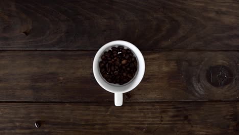 coffee beans falling into cup. top view on wooden table.