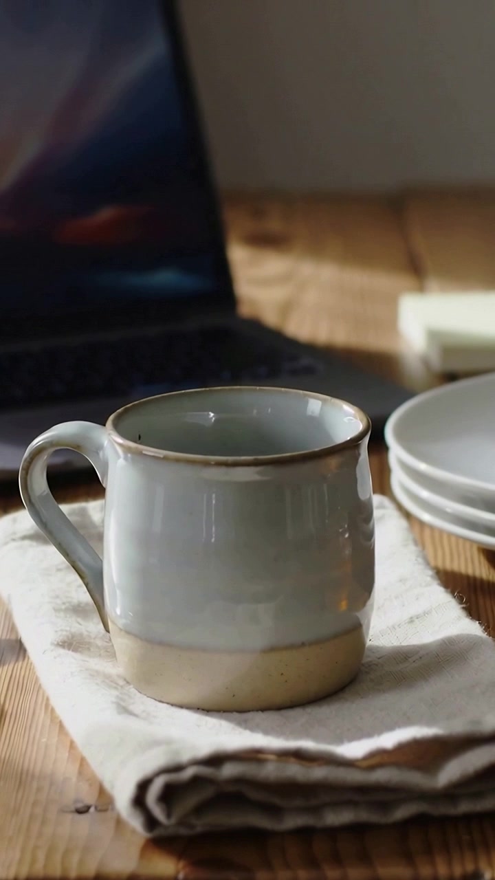 Vertical video: Shifting light casting sheen on mug on linen wood table with laptop plates for work
