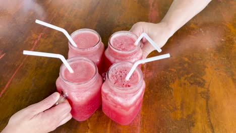 three pink cocktails in mason jars with straws on a wooden table, captured in natural light at a phuket restaurant