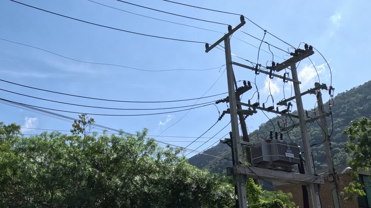 Cropped view of power lines with green foliage and hills under a clear sky.