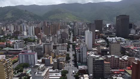 Daytime-reverse-flight-over-Baralt-Avenue,-revealing-downtown-Caracas,-showing-the-city-skyline-against-it's-surrounding-mountain-range