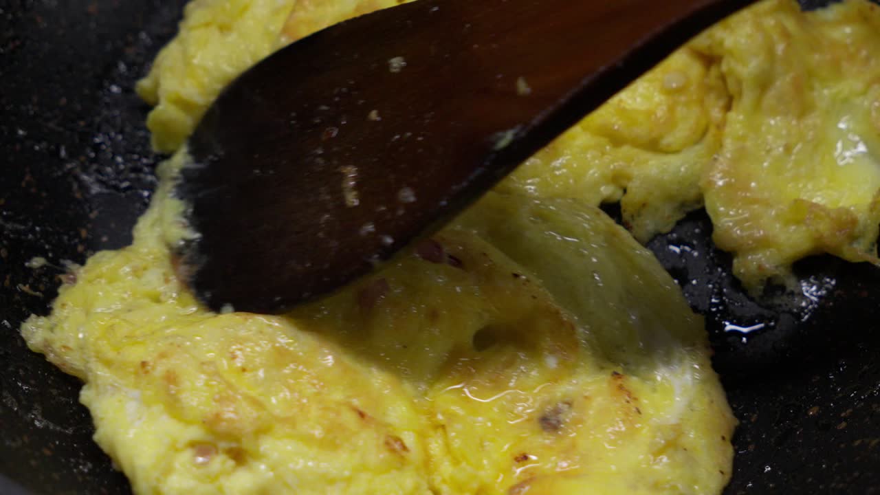 Cooking Scrambled Eggs in Frying Pan with Wooden Spatula, Close-Up