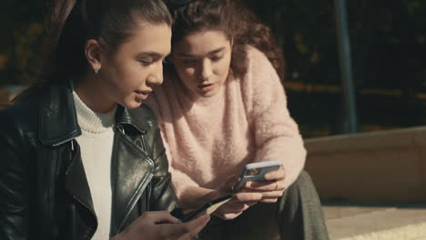 Young-Female-Friends-Using-A-Smartphone-Outdoors