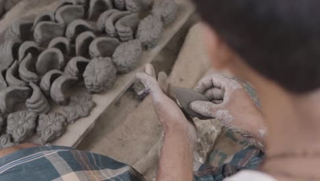 unrecognized poor asian man making idols and sculpture with clay, slow motion over the shoulder shot