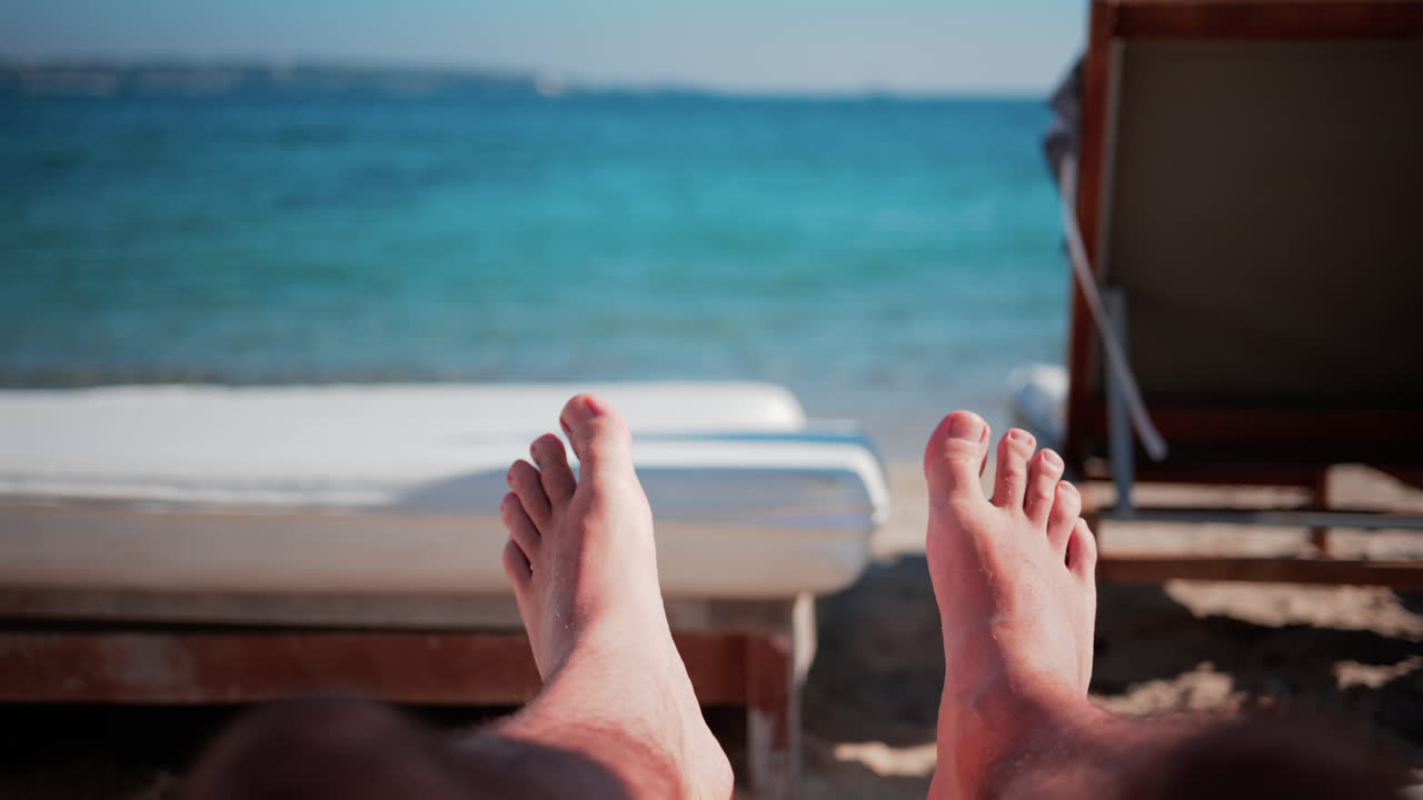 Close up of bare feet resting on a beach lounger with soft sunlight and blurred deck chairs in the background
