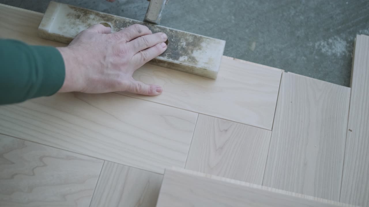 Worker installing wooden flooring with hammer and tapping block