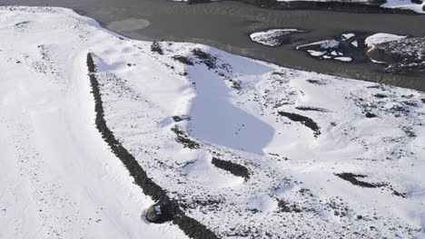 Aerial-establishing-shot-of-a-frozen-lake-and-snowy-surroundings-within-a-mountain-valley