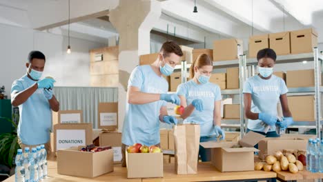 multiethnic group of volunteers in facial mask packing boxes with food and clothes in charity warehouse