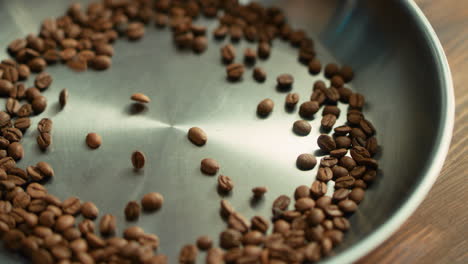 granos de café tostados cayendo sobre la superficie del tazón de metal en cámara lenta.