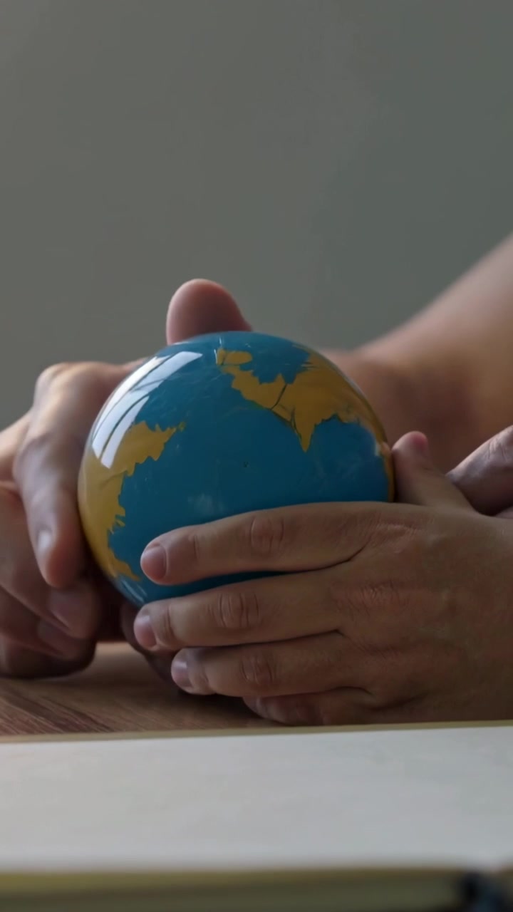 Vídeo vertical: Globo girando sobre a mesa após a mão de cima se deslocar, duas mãos mostrando terras, braços nus