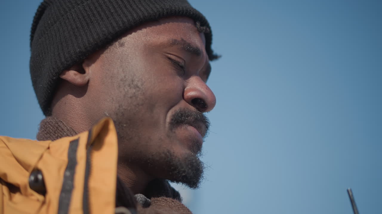close up landscape photographer looking around sipping juice through straw holding digital camera against blur of city buildings and moving cars on snowy street in soft winter daylight