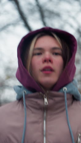 lady in winter outfit jogging briskly through snow-covered outdoor park in urban setting, staying active and warm in cold weather, surrounded by trees with no leaves and chilly urban surrounding