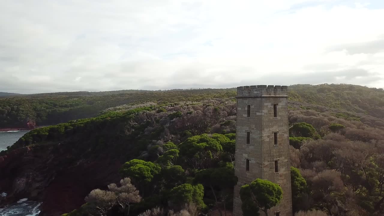 аэрофотосъемка с беспилотника в режиме 360 вокруг заброшенной китобойной вышки, которая возвышается на скалах, а внизу разбиваются волны