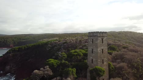 Aerial:-Drone-shot-flying-a-360-around-an-abandoned-whaling-tower-which-is-standing-tall-on-the-cliffs-as-waves-crash-down-below