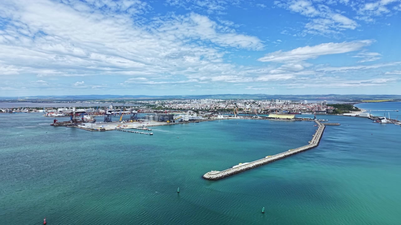 Vista di un porto trafficato situato in una città costiera con aree industriali e cielo azzurro limpido di giorno, che mostra navi e strutture