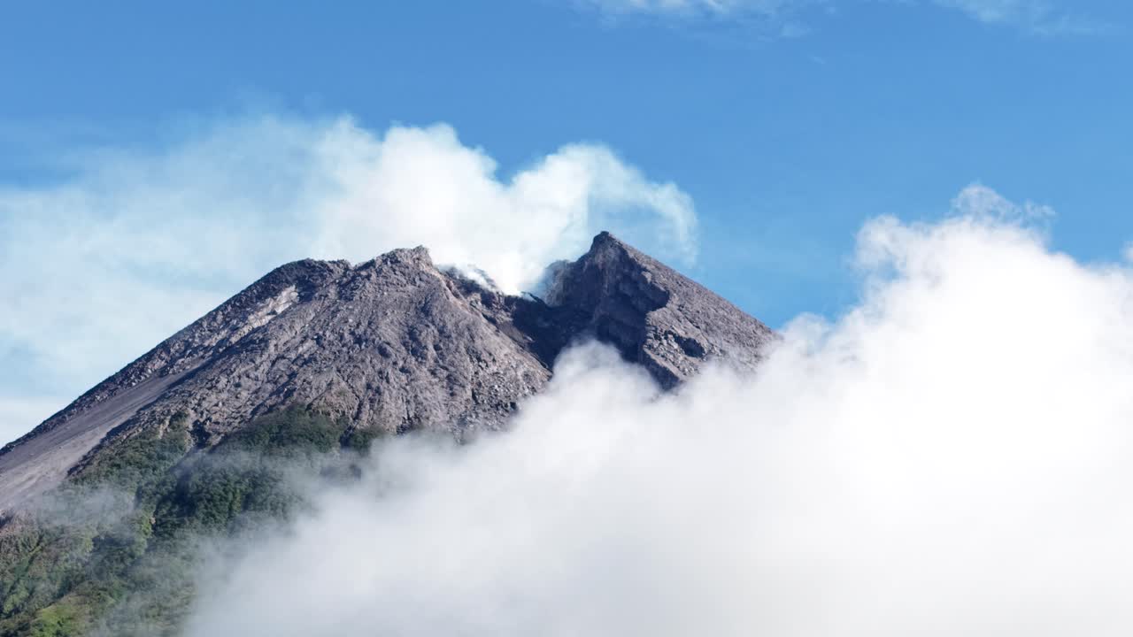 4K-ilmakuvaa Merapi-vuoren huipusta Jogjakartassa, joka on peittynyt paksuihin pilviin, kirkkaan sinisen taivaan alla