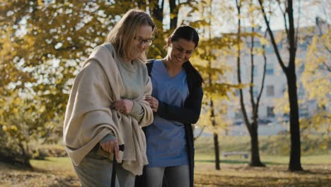 young female nurse helping senior woman walking in park