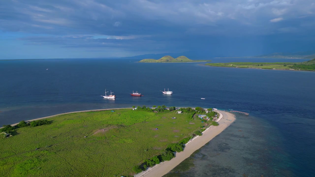 Barche tradizionali ancorate vicino a un'isola verde in una remota baia indonesiana con cielo nuvoloso. Fantastica vista aerea con rotazione panoramica a destra ripresa da drone