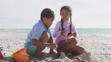 Happy-hispanic-brother-and-sister-playing-on-beach-with-sand