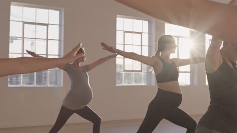 yoga class of healthy pregnant women practicing warrior pose enjoying group physical fitness workout with instructor in studio at sunrise