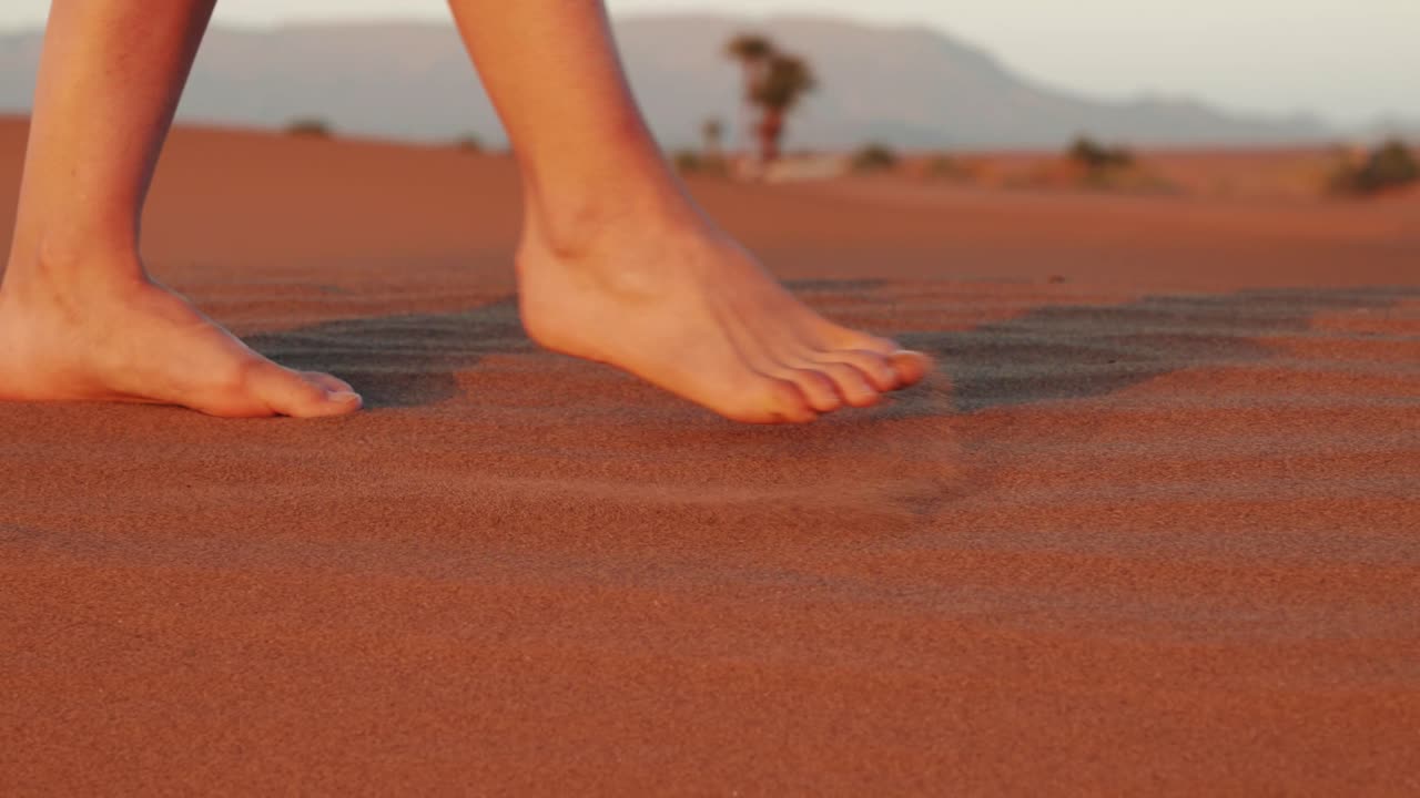 해가 지는 동안 사막에서 모래 위를  ⁇ 고 있는 젊은 백인 여성 다리의 세부 사항