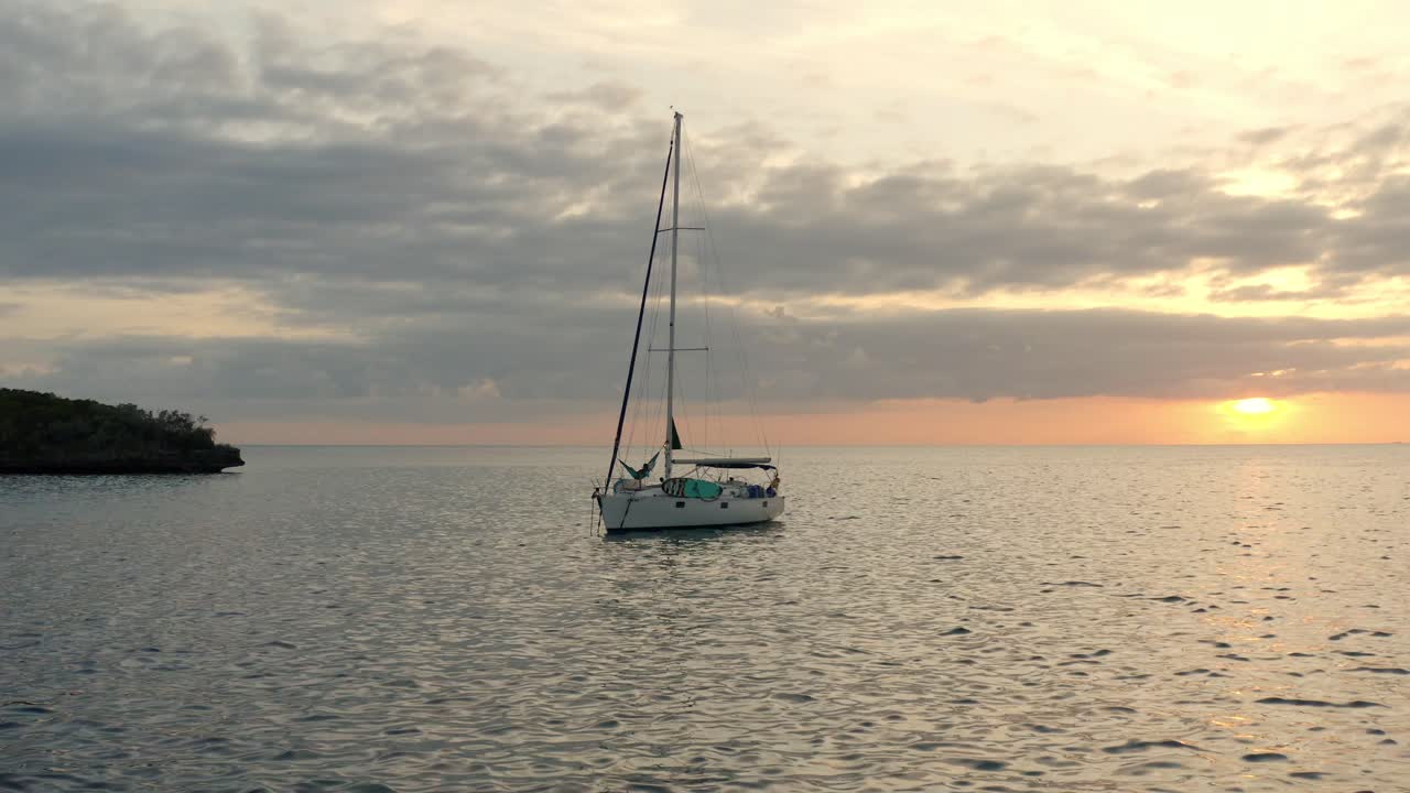velero flotando en el océano con una persona tumbada en una hamaca al atardecer