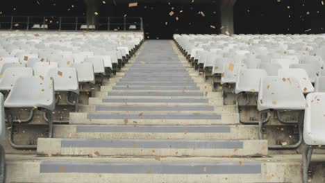 Animation-of-golden-confetti-falling-over-an-empty-rugby-stadium-digital-composition