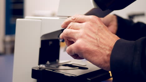 un profesor universitario colocando un portaobjetos de células bajo un microscopio para mostrar a sus alumnos en un laboratorio de biología