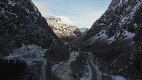 Anorthosite-mining-by-Gudvangen-Stein-seen-close-to-Naeroydal-river-and-road-E16-in-the-valley-of-Gudvangen-Norway---Ascending-aerial-with-bright-sun-in-mountain-background