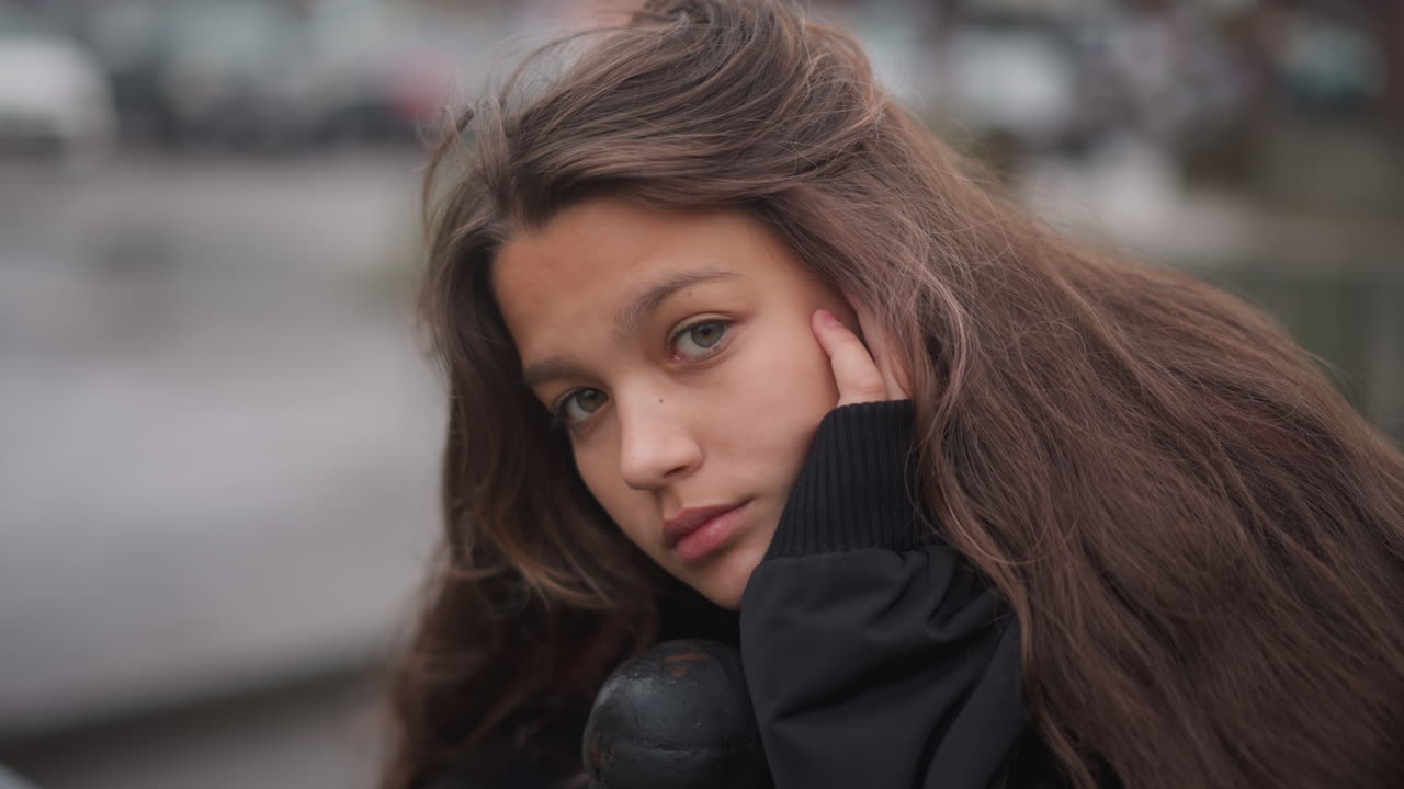 Riflessione cupa e piovosa. Una donna pensierosa guarda l'acqua. Una donna riflessiva fissa pensierosamente le pozzanghere di pioggia. Una donna seria osserva la sua immagine riflessa nell'acqua piovosa con contemplazione.