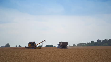 yellow harvester machine stopped in the field and combiner examining it from outside. tractor approaching the harvester to upload the crops.