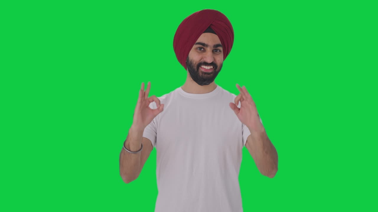hombre indio sikh feliz mostrando la pantalla verde de la señal de ok