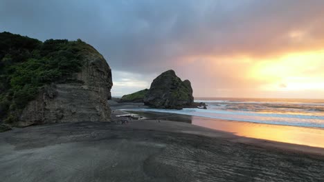 flying towards the taitomo island and taitomo rock from piha beach during golden hour in auckland, new zealand