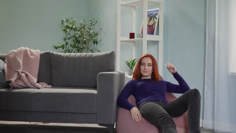 red-haired housewife comes to sit on pouf chair to rest