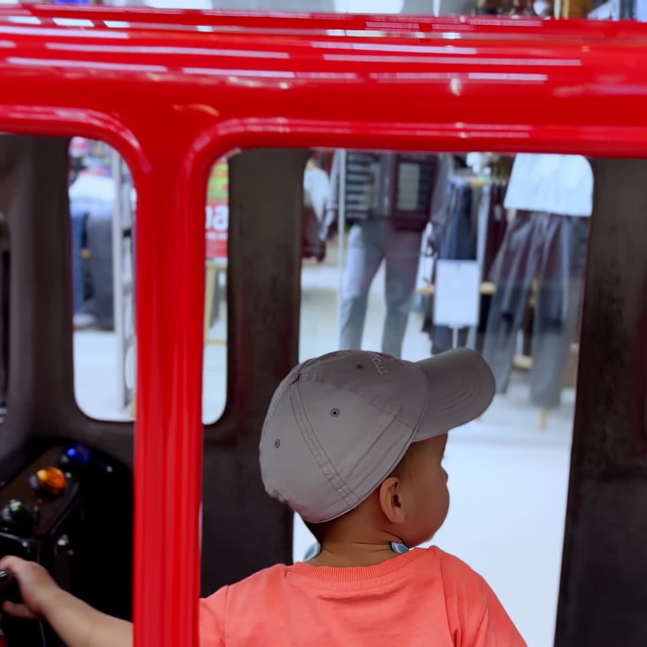 Adorable baby boy face peeping from the red toy car he's sitting in. Toddler pays inside the fire machine