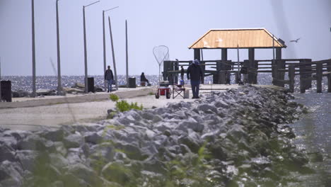 a diverse group of people fish on the foot of a broken pier